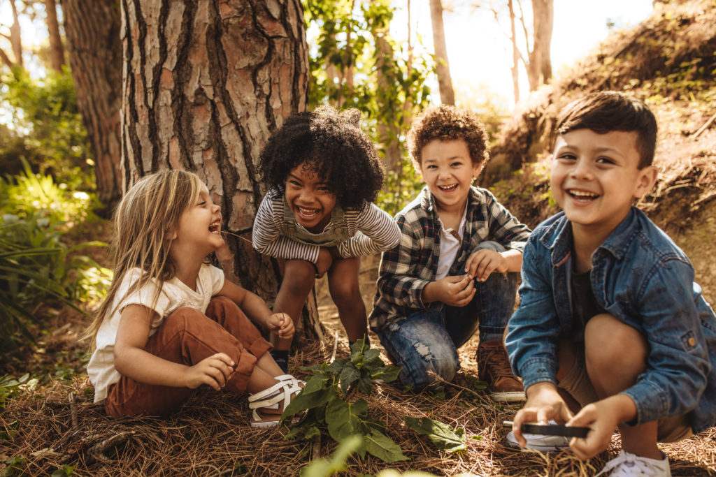 Group of cute kids sitting together in forest and looking at camera. Cute children playing in woods.